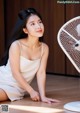 A woman in a white dress sitting on the floor next to a fan.