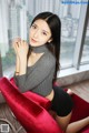 A woman sitting on a red chair in front of a window.