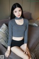 A woman sitting on a couch wearing a gray sweater and black shorts.