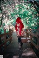 A woman in a red riding hoodie walking across a wooden bridge.