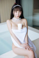 A woman in a white towel sitting on a bathtub with a cup of coffee.