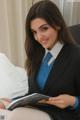 A woman in a business suit sitting on a bed reading a magazine.