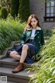 A woman sitting on the steps of a building wearing a green coat.