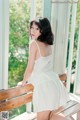 A woman in a white dress sitting on a wooden bench.