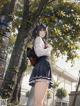 A girl in a school uniform standing next to a tree.