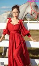 A woman in a red dress standing next to a white horse.