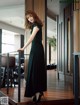 A woman in a long black dress standing on a wooden floor.