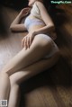 A woman in a white lingerie sitting on a wooden floor.