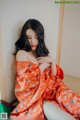 A woman in an orange kimono sitting on a bed.