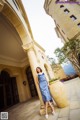 A woman in a blue dress standing in front of a tall building.